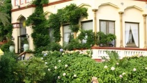 Een gebouw in klassieke stijl, met een symmetrische gevel, grote ramen en een verzorgde tuin met diverse planten en bloemen.