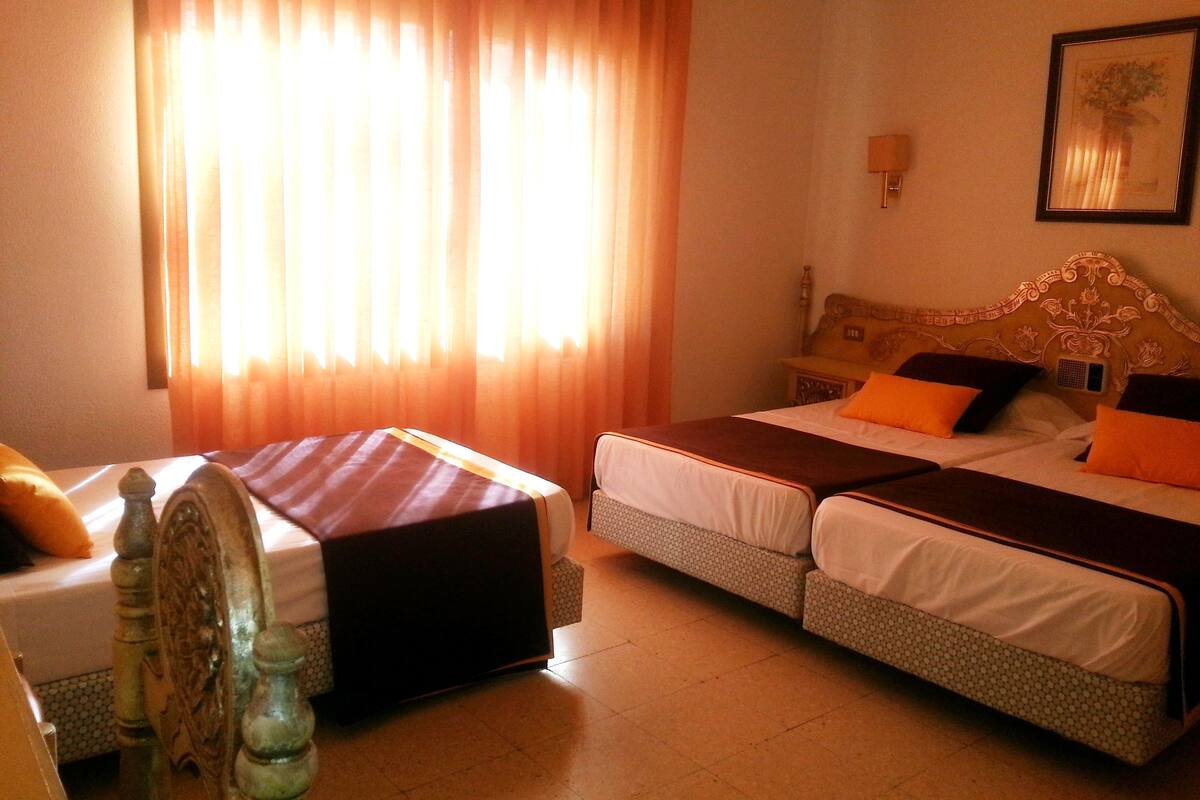 Una habitación de hotel con dos camas, cabecero de madera y un ventanal con cortinas.