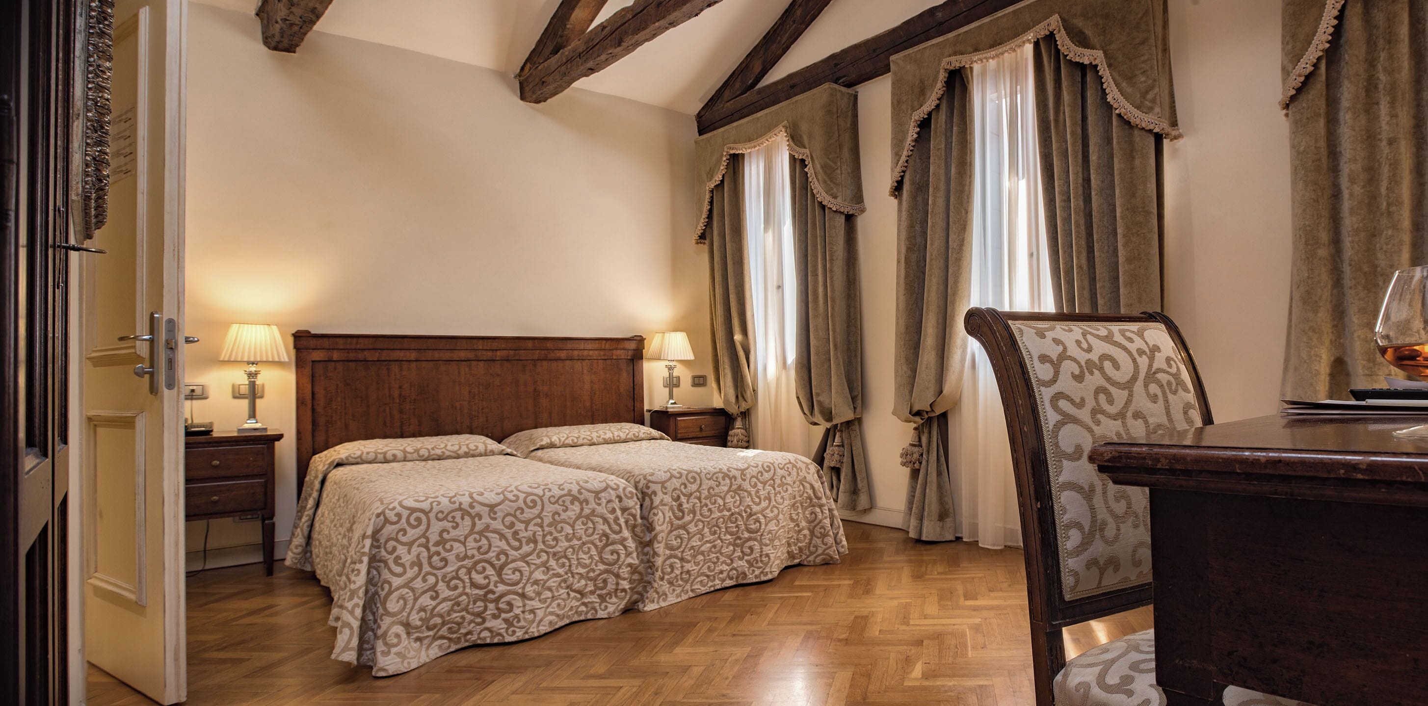 Une chambre à coucher avec une tête de lit en bois, deux lits avec une literie à motifs, une table de chevet avec des lampes et une chaise.