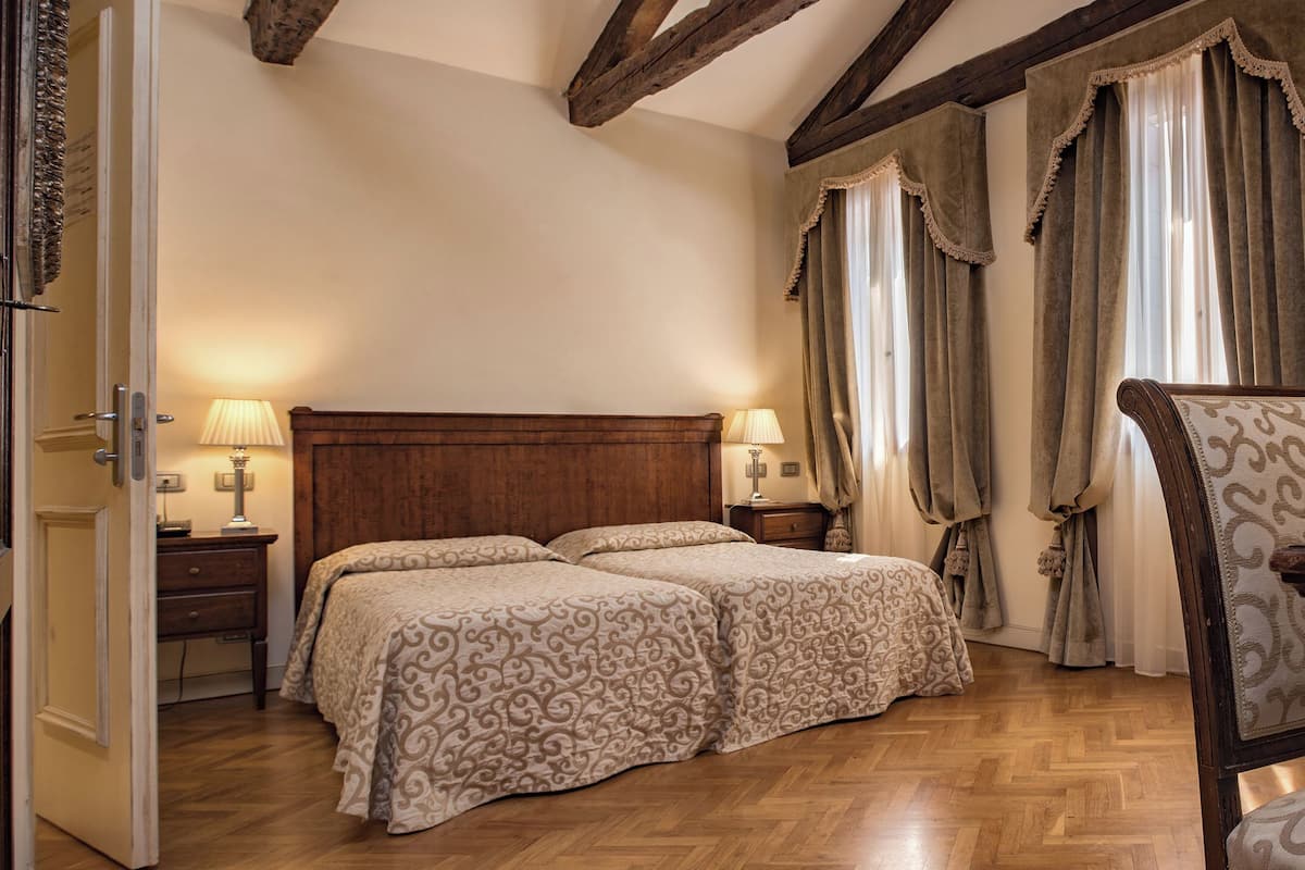 Une chambre à coucher avec une tête de lit en bois, deux lits avec une literie à motifs, une table de chevet avec des lampes et une chaise.