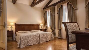 Un dormitorio con cabecera de madera, dos camas con ropa de cama estampada, una mesita de noche con lámparas y una silla.