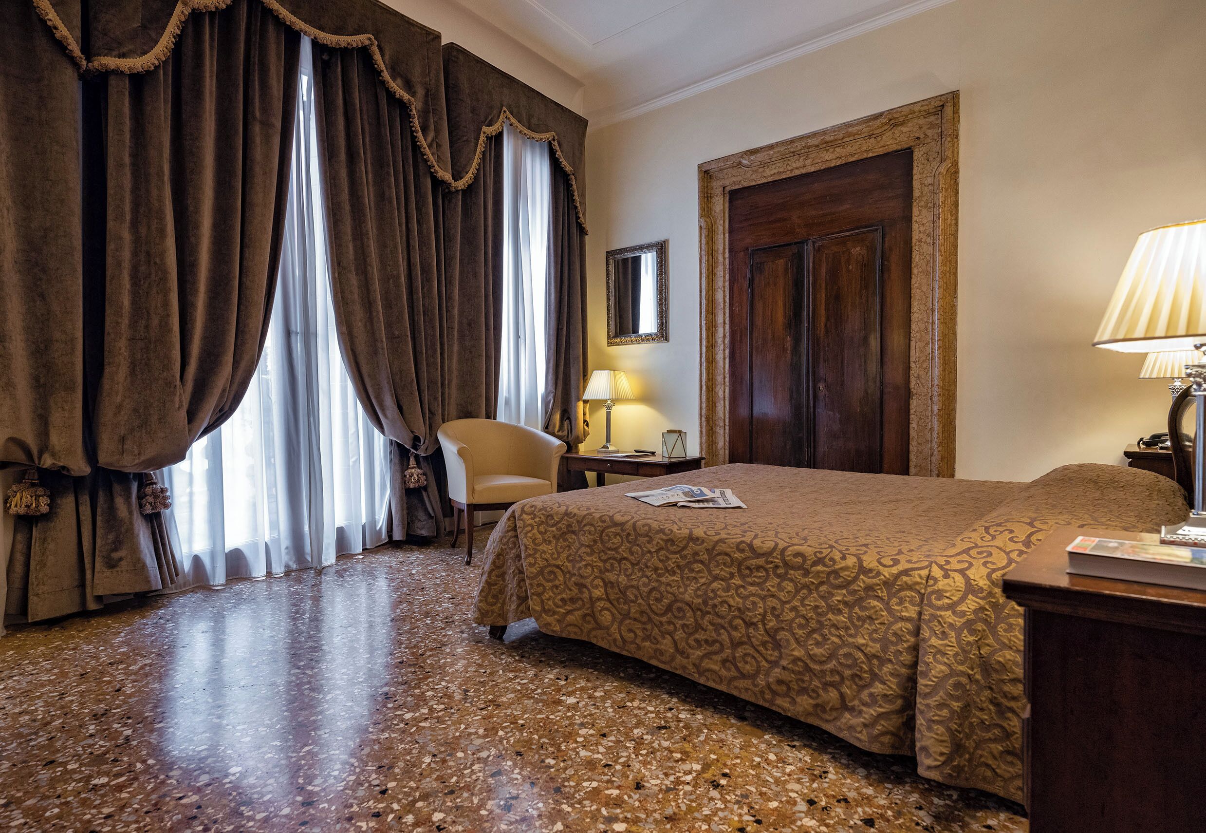 Une chambre d’hôtel avec un grand lit, une chaise, un bureau avec une lampe et une porte.