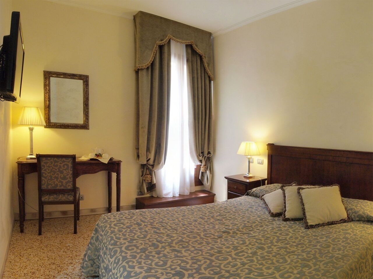Een hotelkamer met een bed, een bureau, een stoel, een nachtkastje en een lamp.