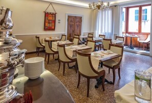 A dining area with tables set for service, a buffet station, and a view of the outside through large windows. - Hotel Dell'Opera (Venice)