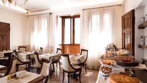 Un espace repas comprenant plusieurs tables et chaises, un buffet proposant divers plats, et une grande fenêtre agrémentée de rideaux.