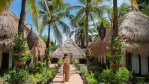 A pathway lined with thatched-roof huts, surrounded by lush greenery and palm trees. - Dhevan Dara Resort & Spa (Hua Hin)