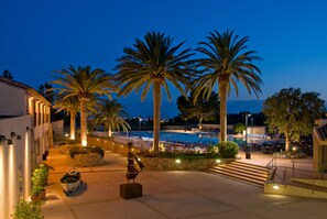 A poolside area with palm trees, outdoor seating, and a view of the sea at dusk. - Hotel San Carlos (Roses)