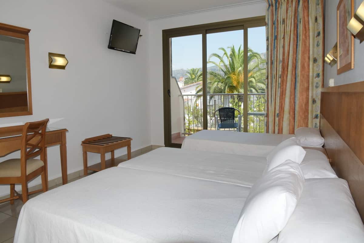 Habitación de hotel con una cama grande, un escritorio con silla, televisión montada en la pared y un balcón con vistas a palmeras.