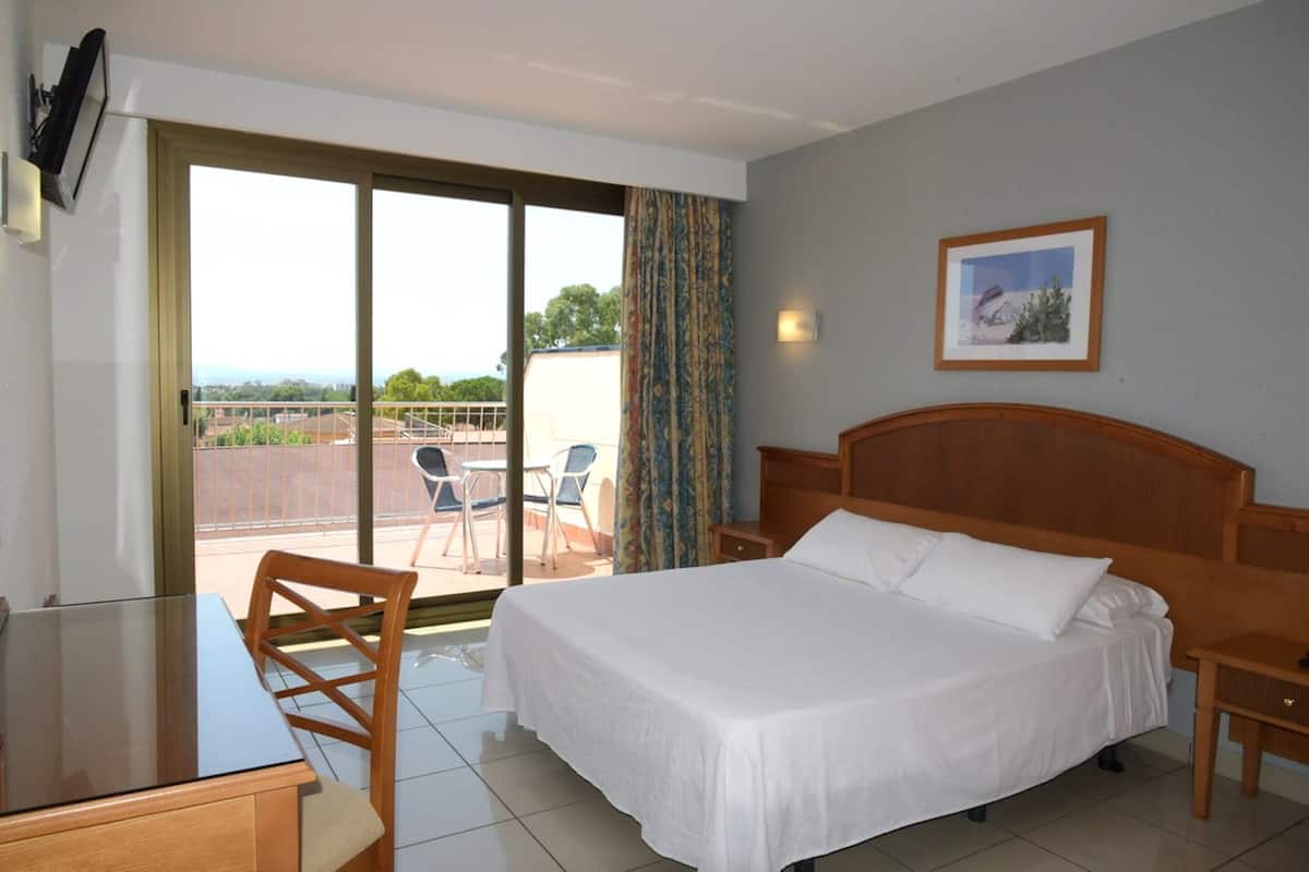 Habitación de hotel con cama, escritorio y silla. Tiene un balcón con vista a la ciudad.