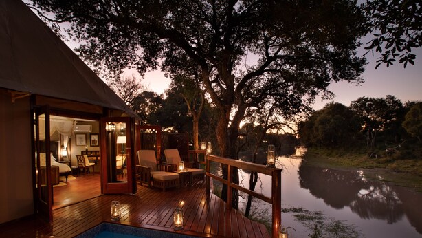 A wooden deck with a pool, surrounded by trees and a calm body of water. - Hamiltons Tented Camp (Bushbuckridge)