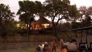 A lodge with a dining area by a lake, surrounded by trees. - Hamiltons Tented Camp (Bushbuckridge)