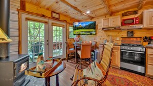 A cozy cabin interior with a wood stove, dining area, kitchen, and a large window overlooking a scenic landscape. - Creekwalk Inn and Cabins (Cosby)