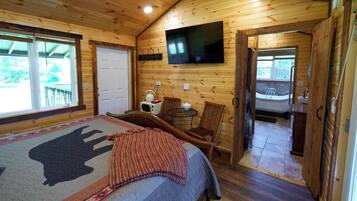 A wooden cabin room with a bed, a TV, a small table, and a chair.