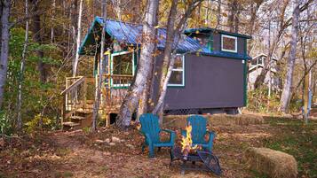 A cabin with a deck, two chairs, and a fire pit.