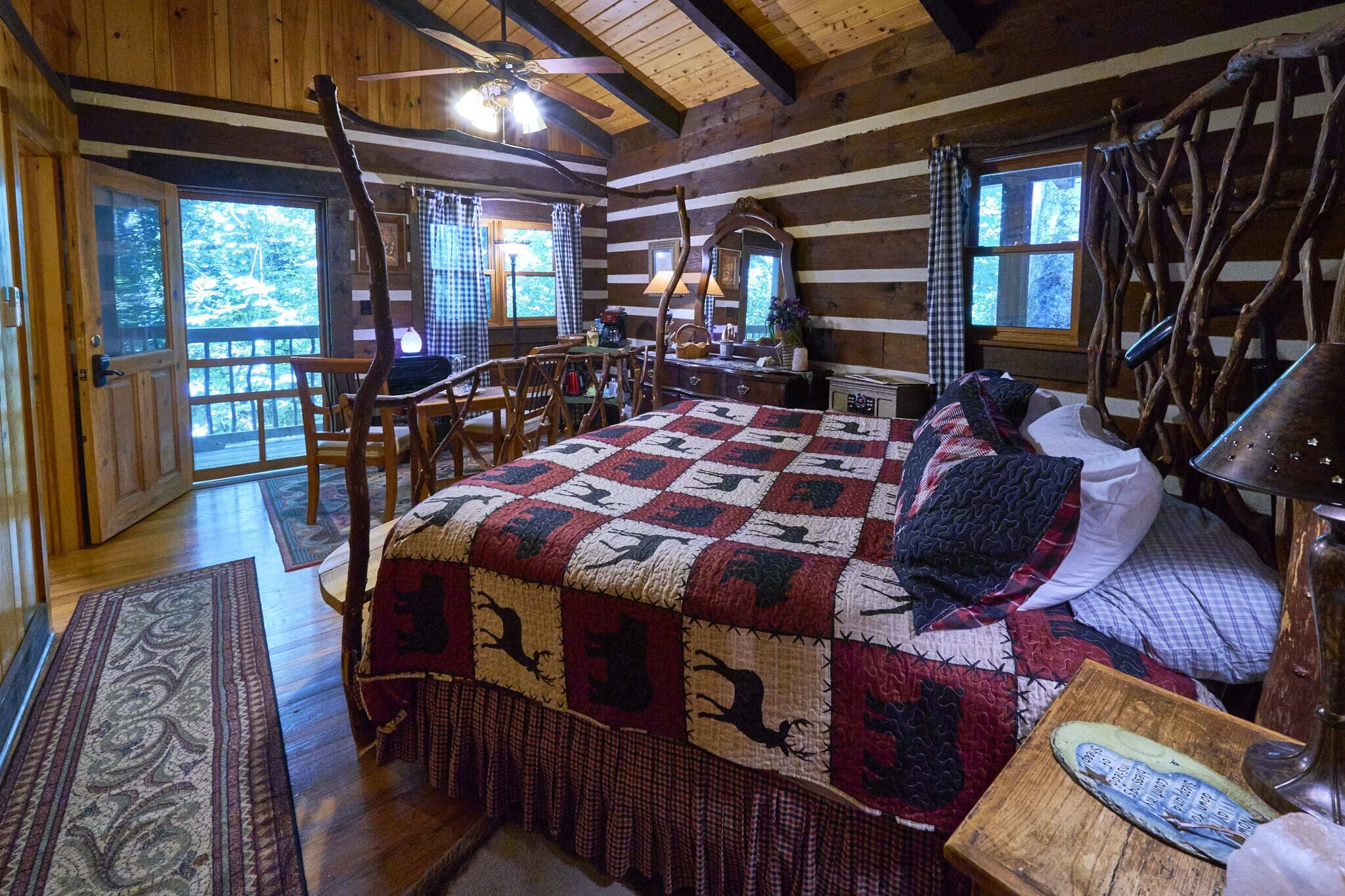 A log cabin bedroom with a large bed, wooden furniture, and a view of the outdoors.