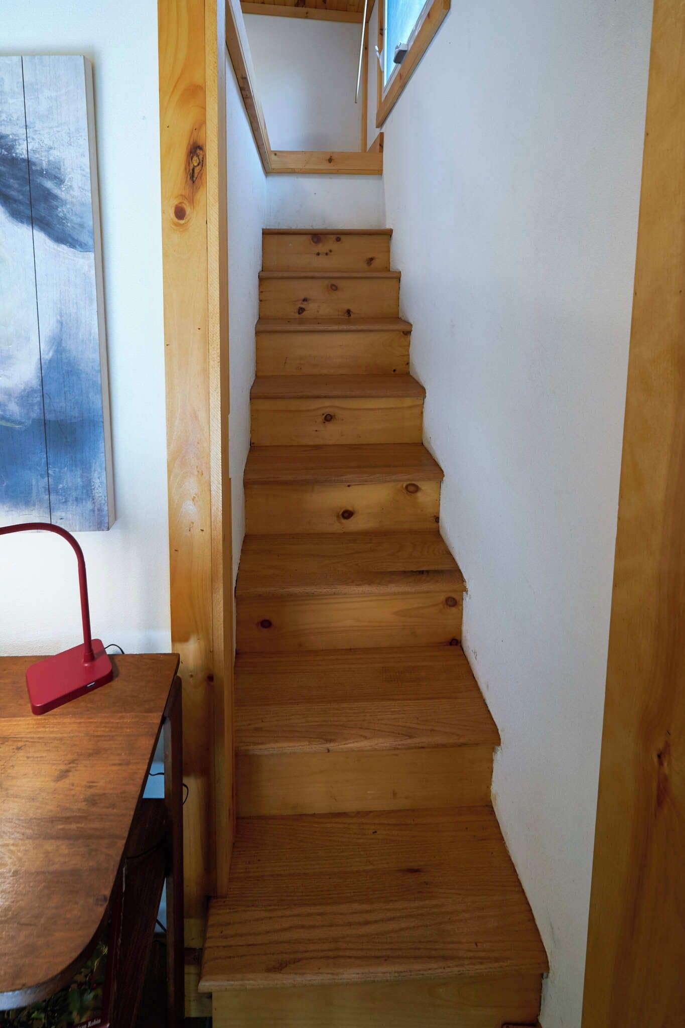 A wooden staircase with a red object on a table at the bottom.