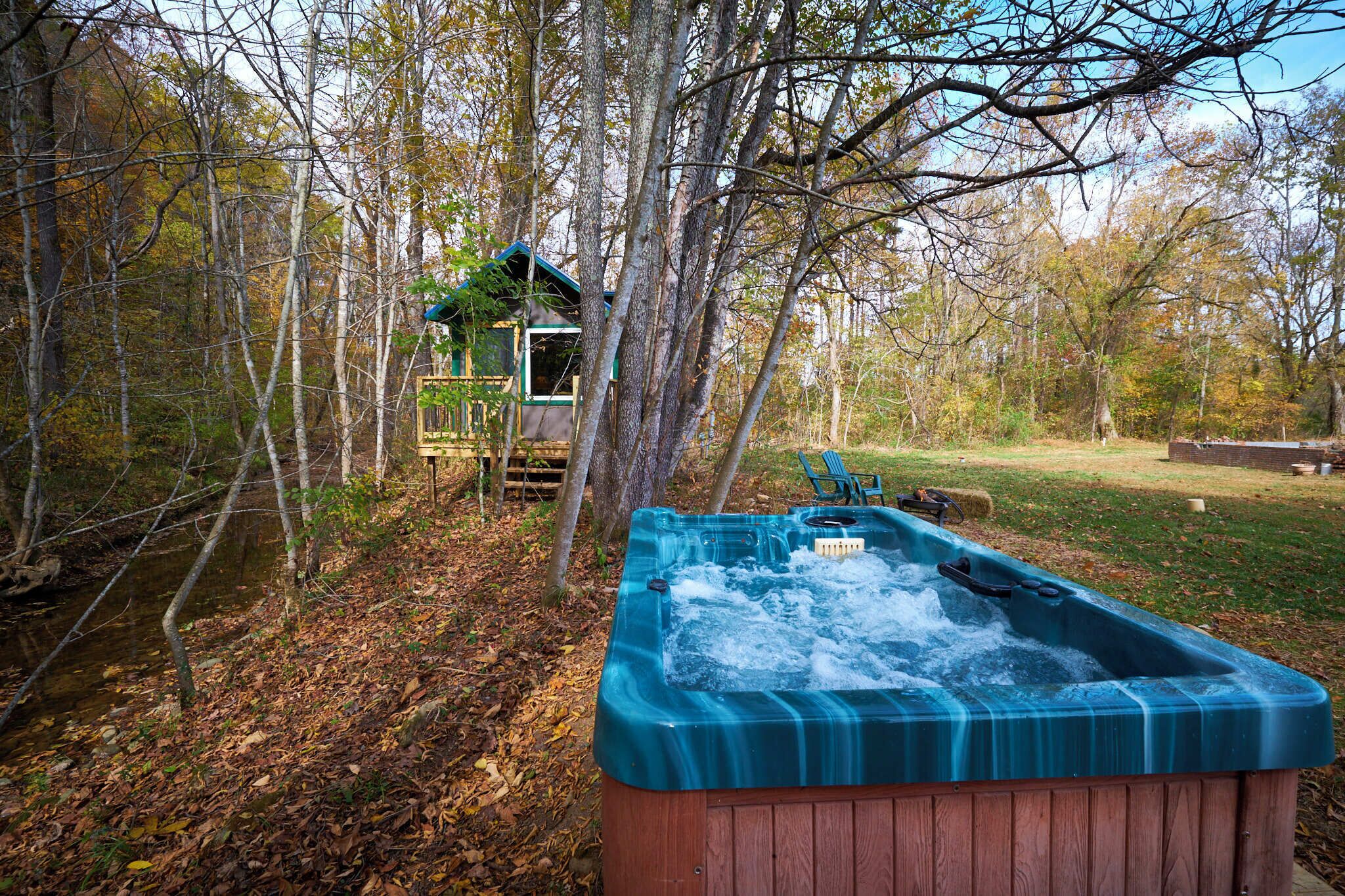 A hot tub in a wooded area with a small cabin in the background.