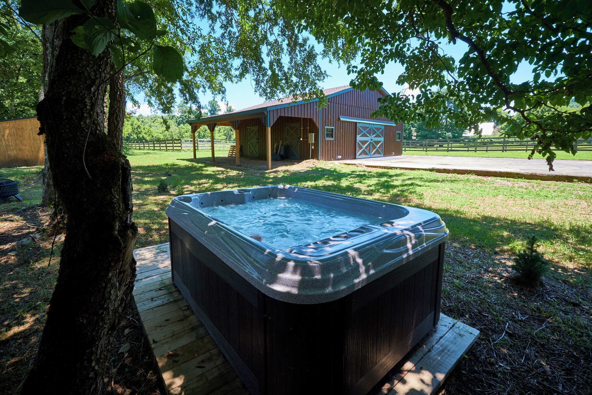 A hot tub on a wooden deck with a barn and covered structure in the background.