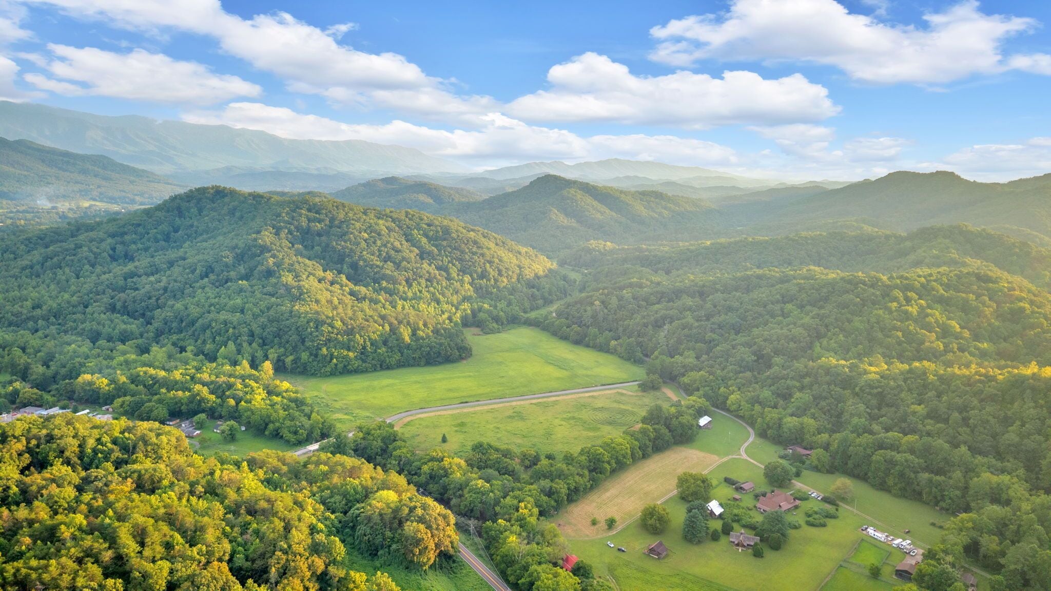 Un paisaje rural con colinas ondulantes, un camino sinuoso y casas dispersas.