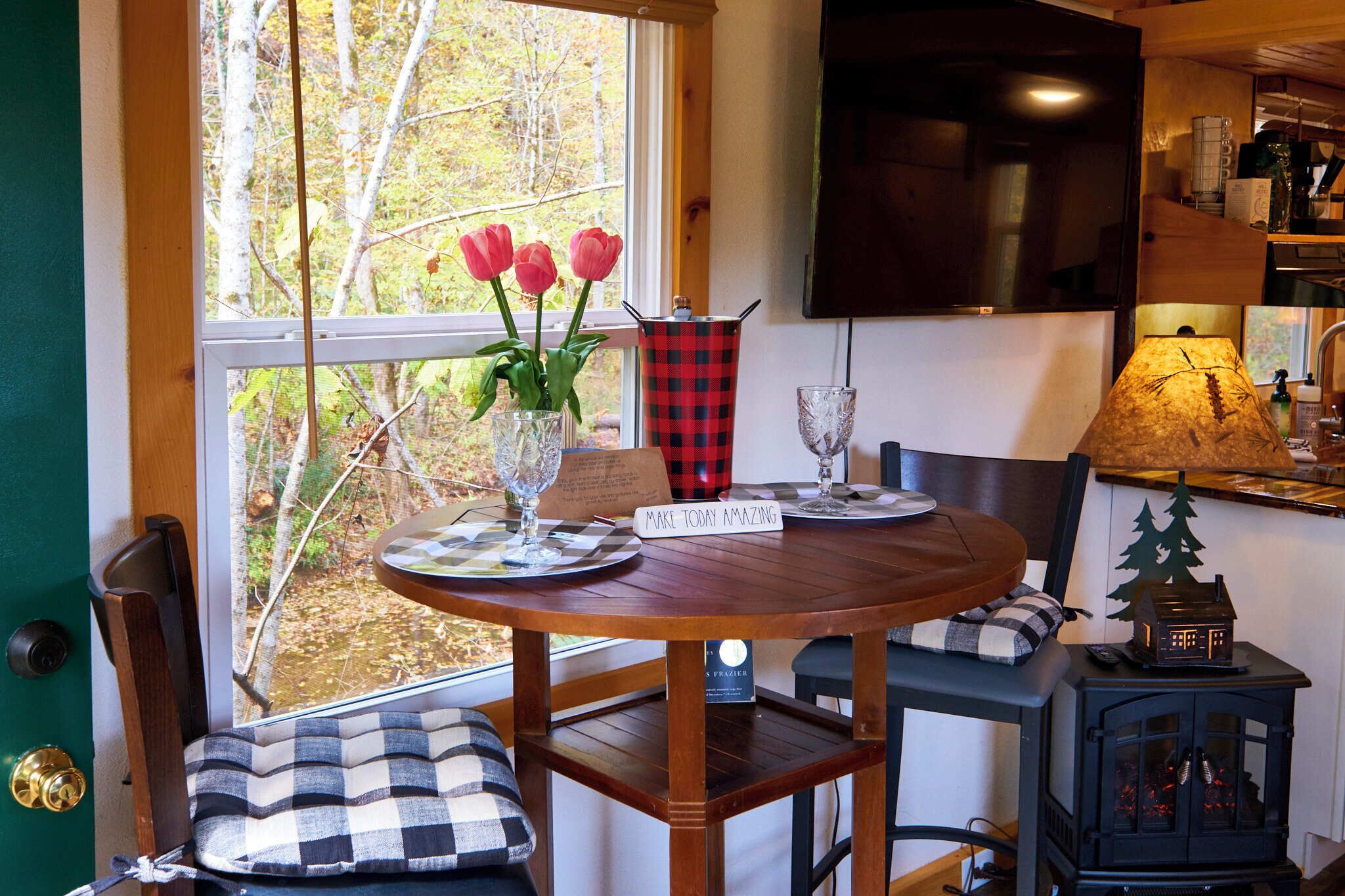 A cozy dining area with a wooden table, chairs, a vase with flowers, a plaid table runner, and a sign that reads "MAKE TODAY AMAZING".