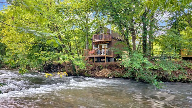 A wooden cabin with a deck, surrounded by dense forest and a flowing river. - Creekwalk Inn and Cabins (Cosby)