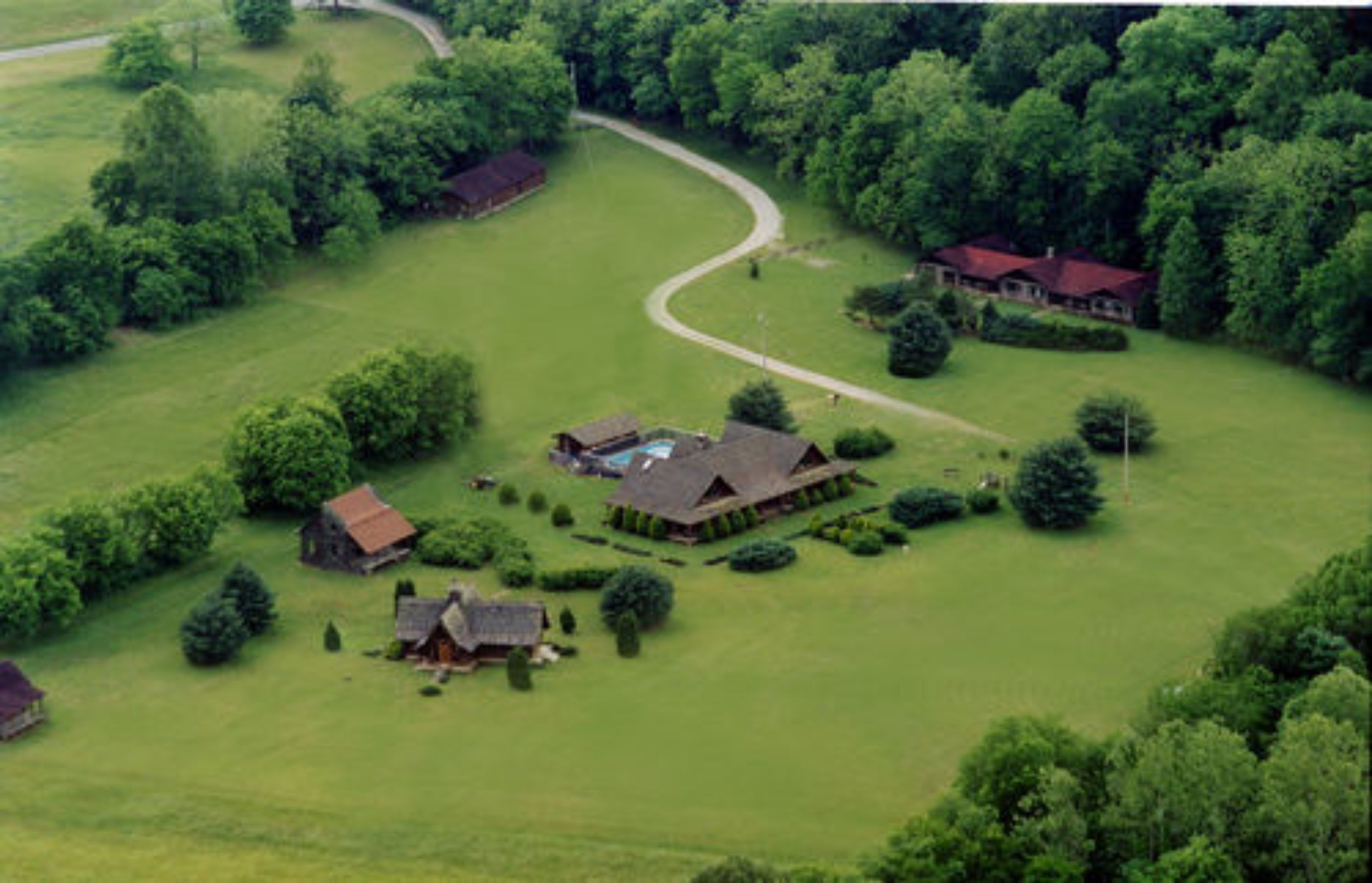 An aerial view of a rural property with a large house, smaller buildings, and a well-maintained lawn.