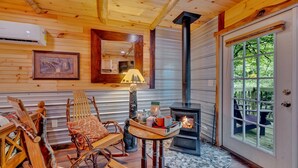A cozy cabin interior with a wood-burning stove, rustic furniture, and a large window overlooking greenery. - Creekwalk Inn and Cabins (Cosby)