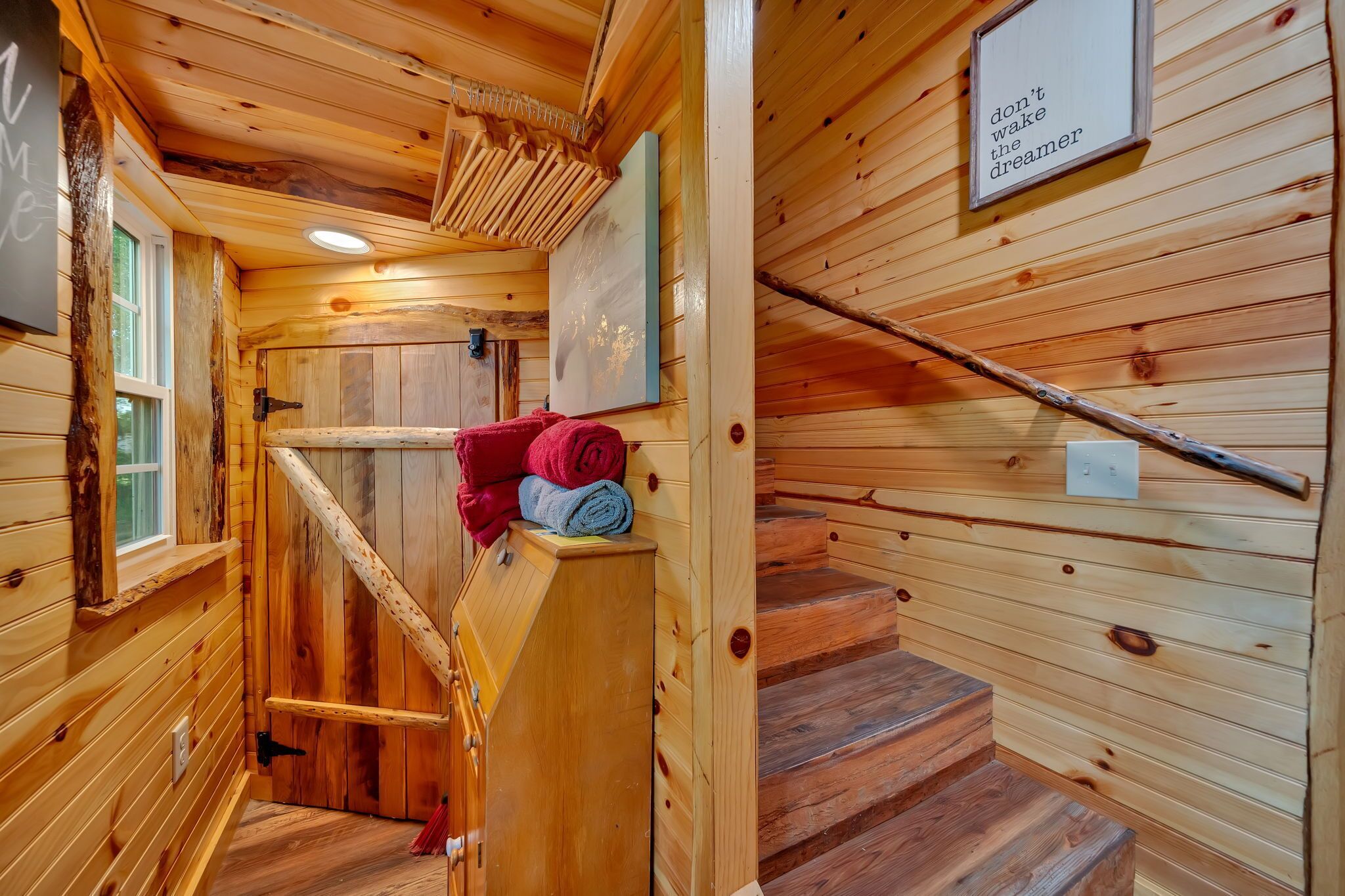 A wooden interior with a staircase, a wall-mounted sign, and a window.
