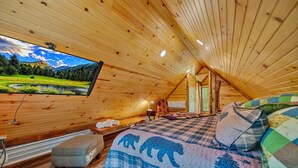 A cozy attic bedroom with wooden walls, a large TV displaying a scenic landscape, a bed with a quilted blanket, and a small bench. - Creekwalk Inn and Cabins (Cosby)