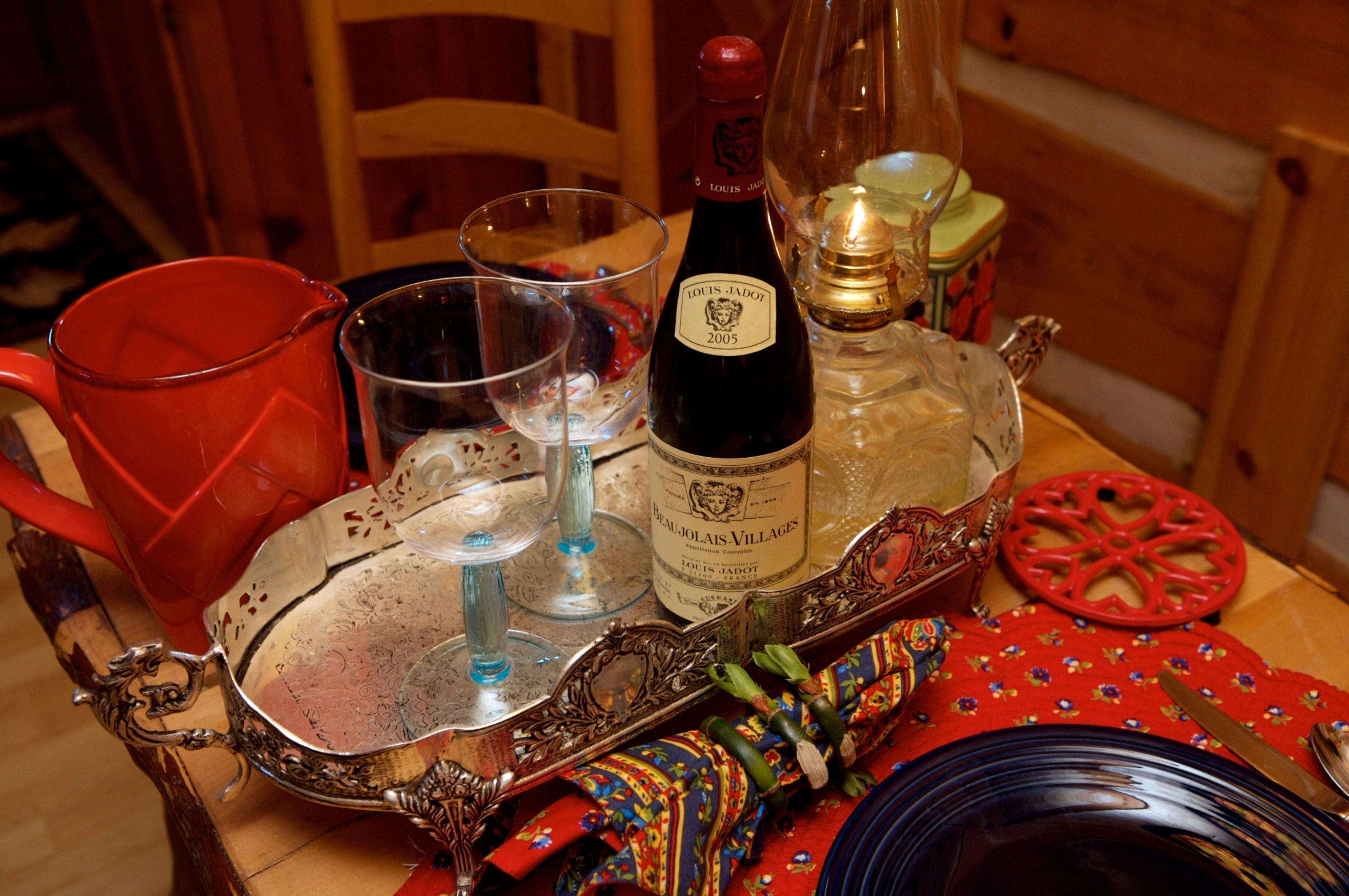 Un tavolo con una bottiglia di vino, bicchieri, una tazza rossa e un vassoio decorativo.