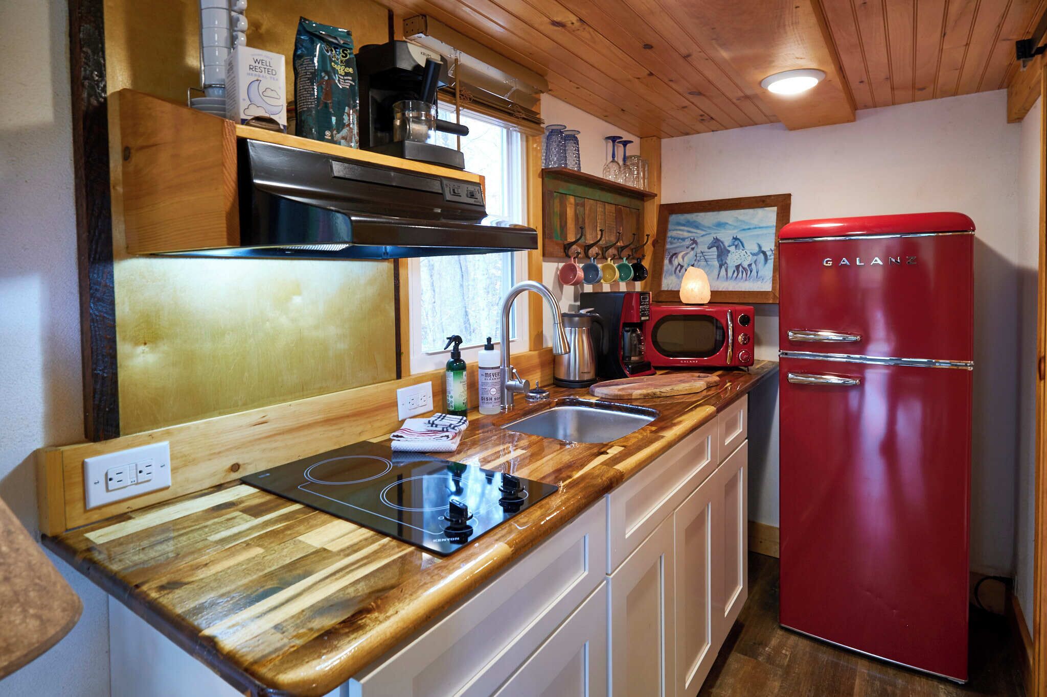 A kitchen with a red refrigerator, wooden countertops, a sink, and a stove.