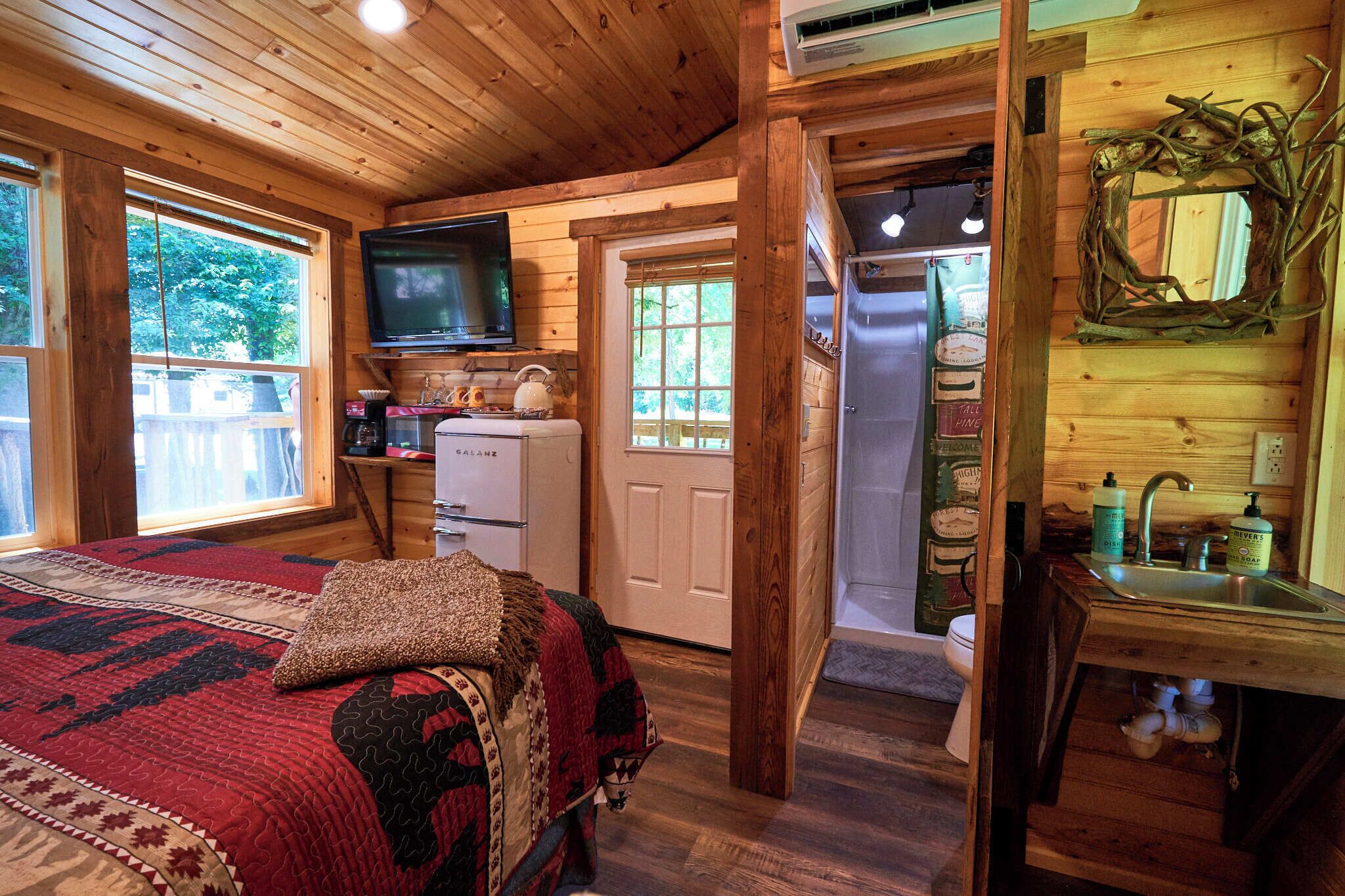 A cozy cabin interior with a bed, a television, a kitchenette, and a bathroom.