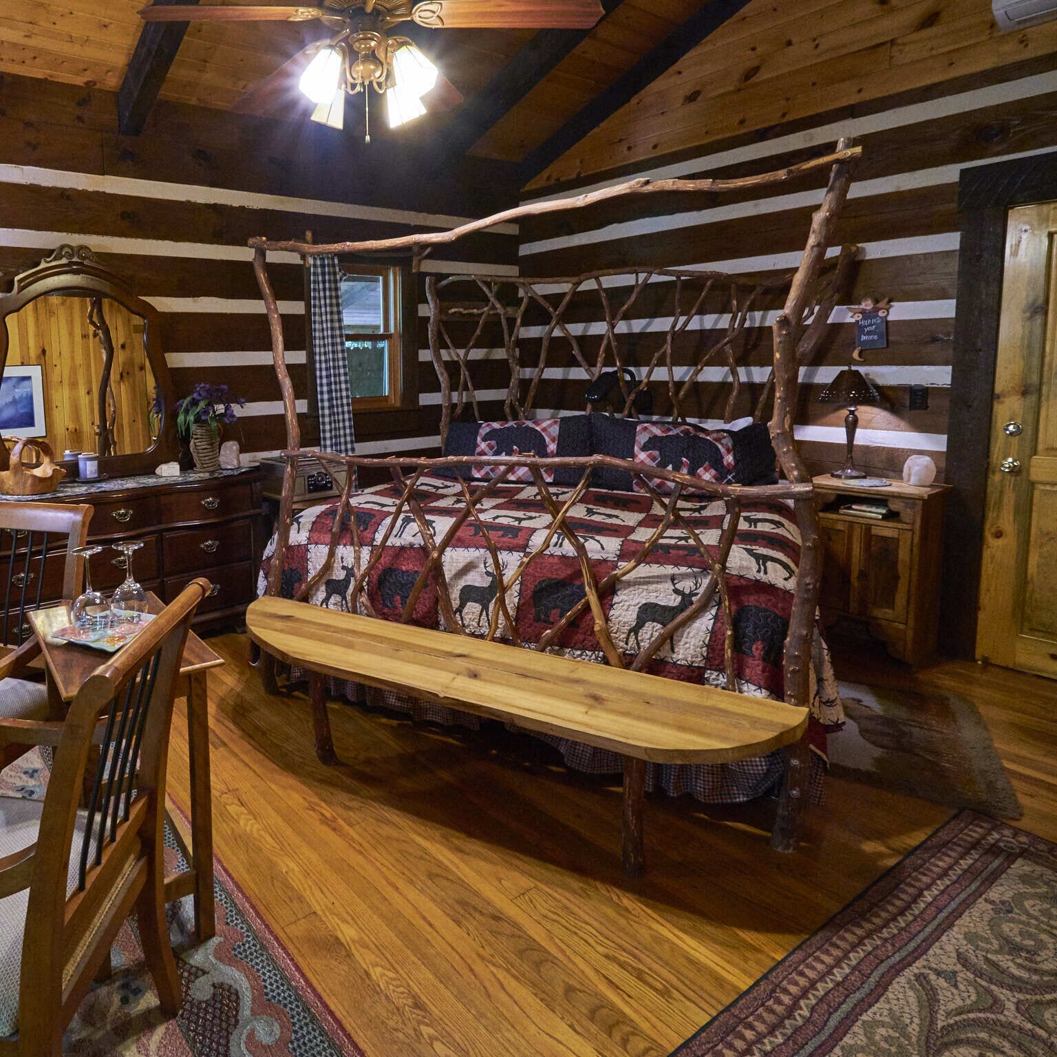 A rustic cabin bedroom with a four-poster bed, wooden furniture, and a ceiling fan.