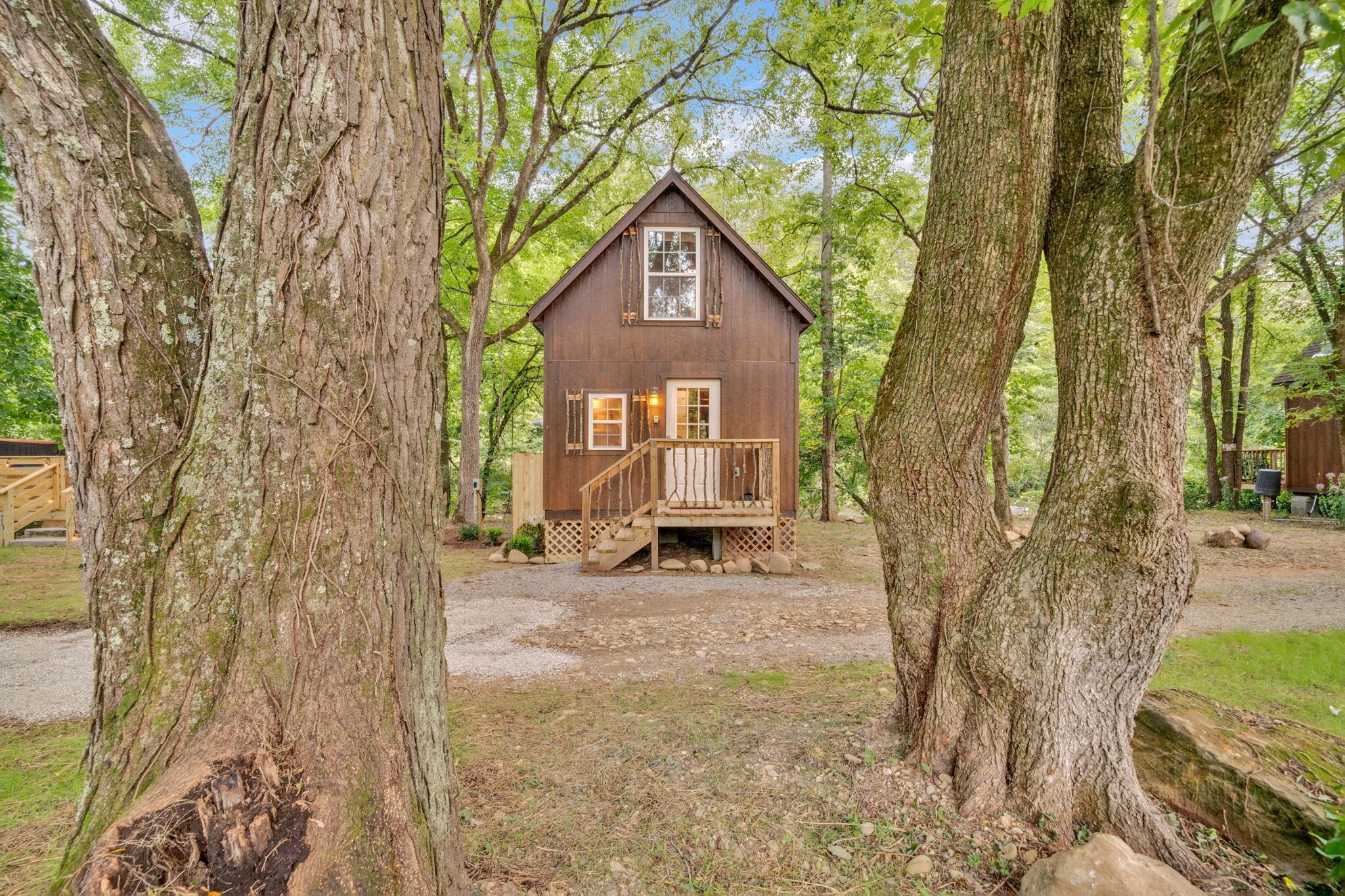 A rustic cabin with a wooden deck, surrounded by large trees.