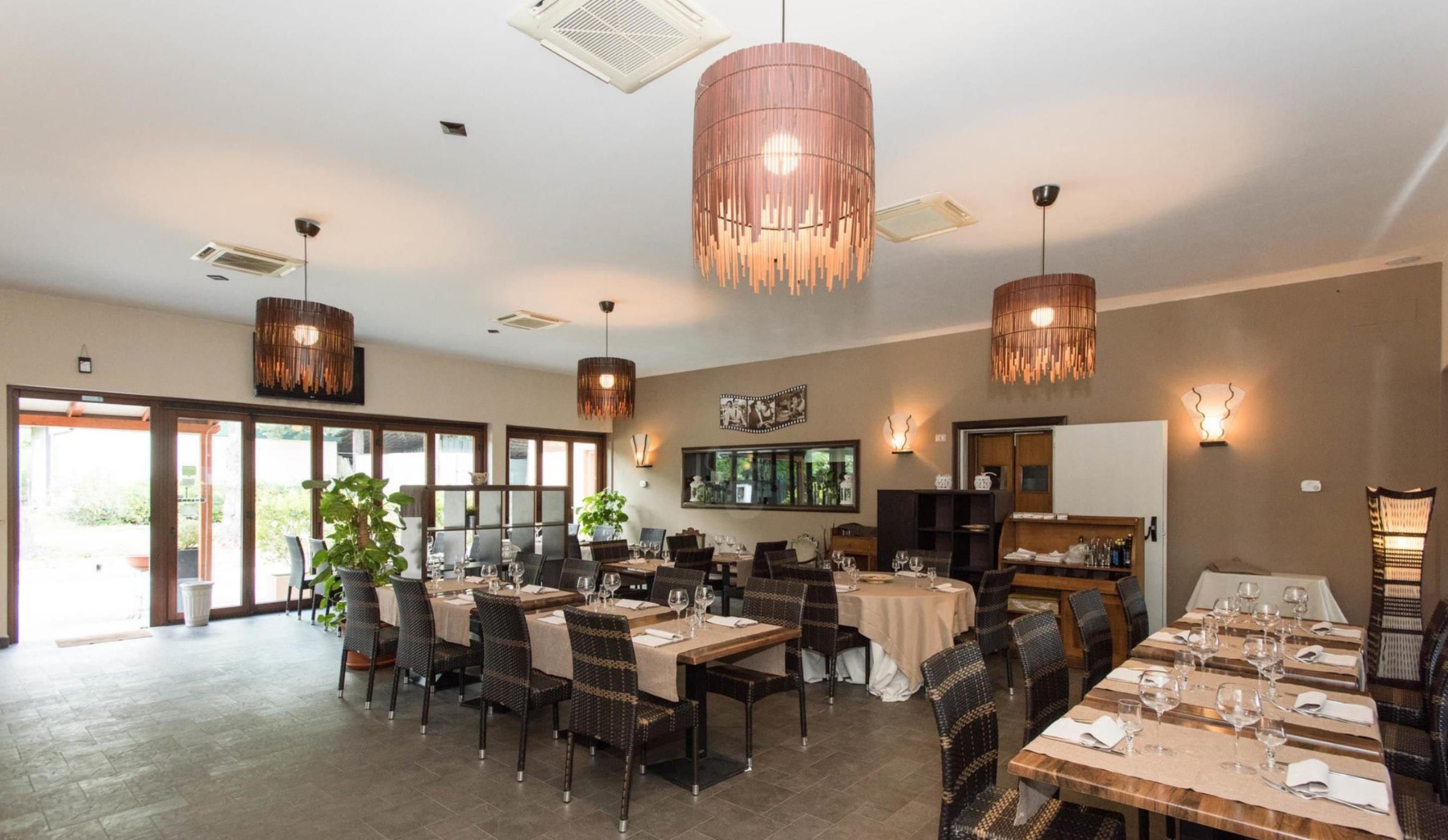 Un vaste espace dédié à la salle à manger, avec de nombreuses tables et chaises, de grands luminaires suspendus et une grande fenêtre qui laisse entrer la lumière naturelle.