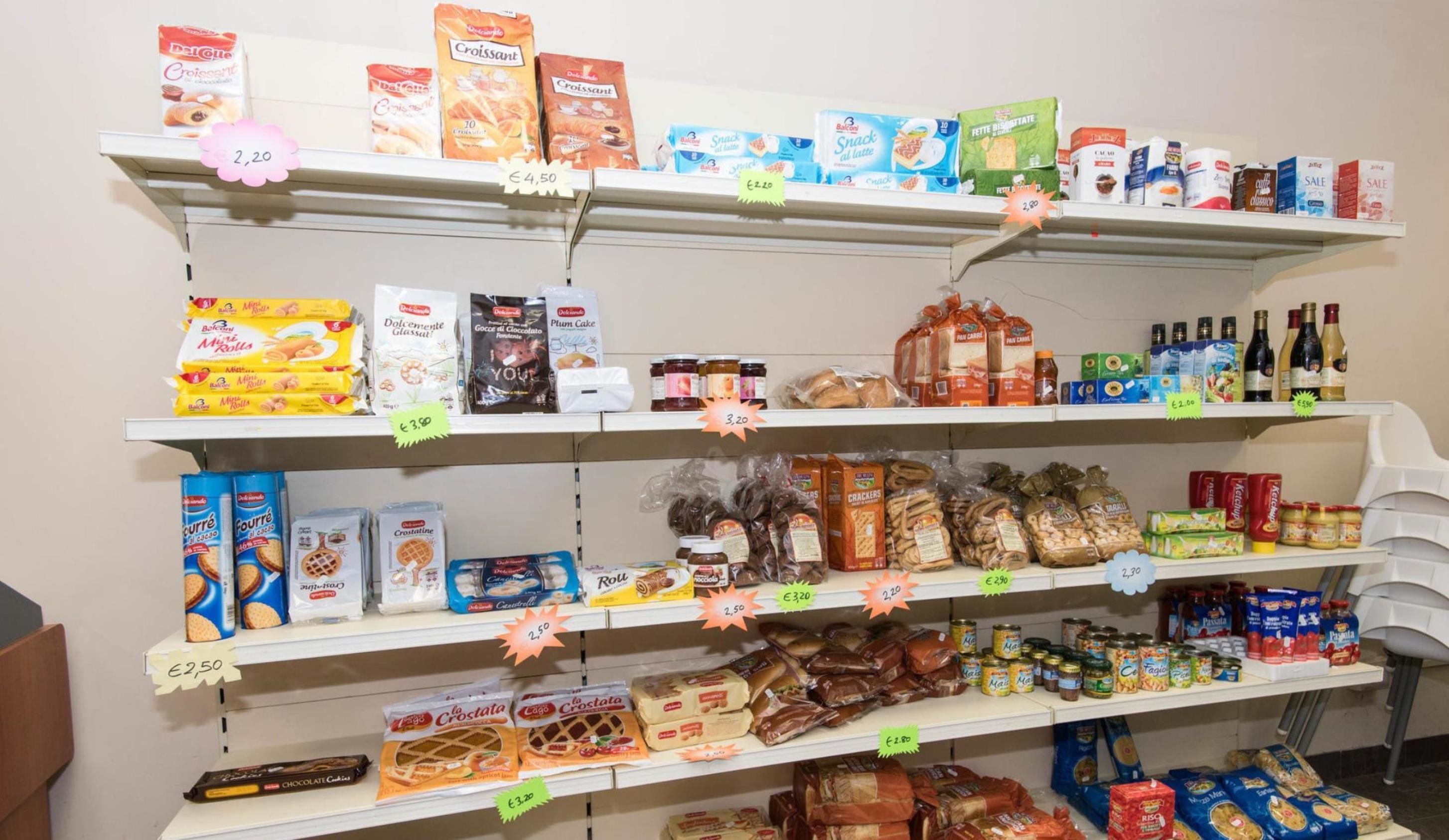 Uno scaffale di un negozio di alimentari pieno di diversi prodotti alimentari e bevande, tra cui snack, pane e latticini.