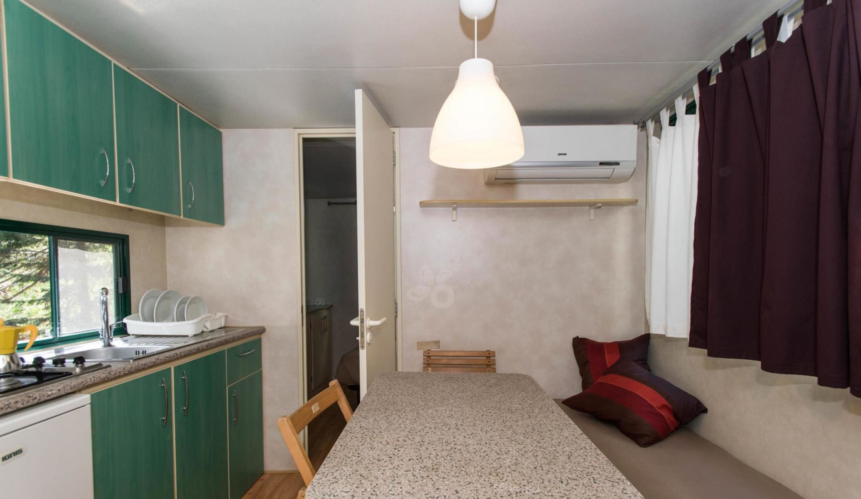 A compact room with a kitchenette, a dining table, a single bed, and a ceiling fan.