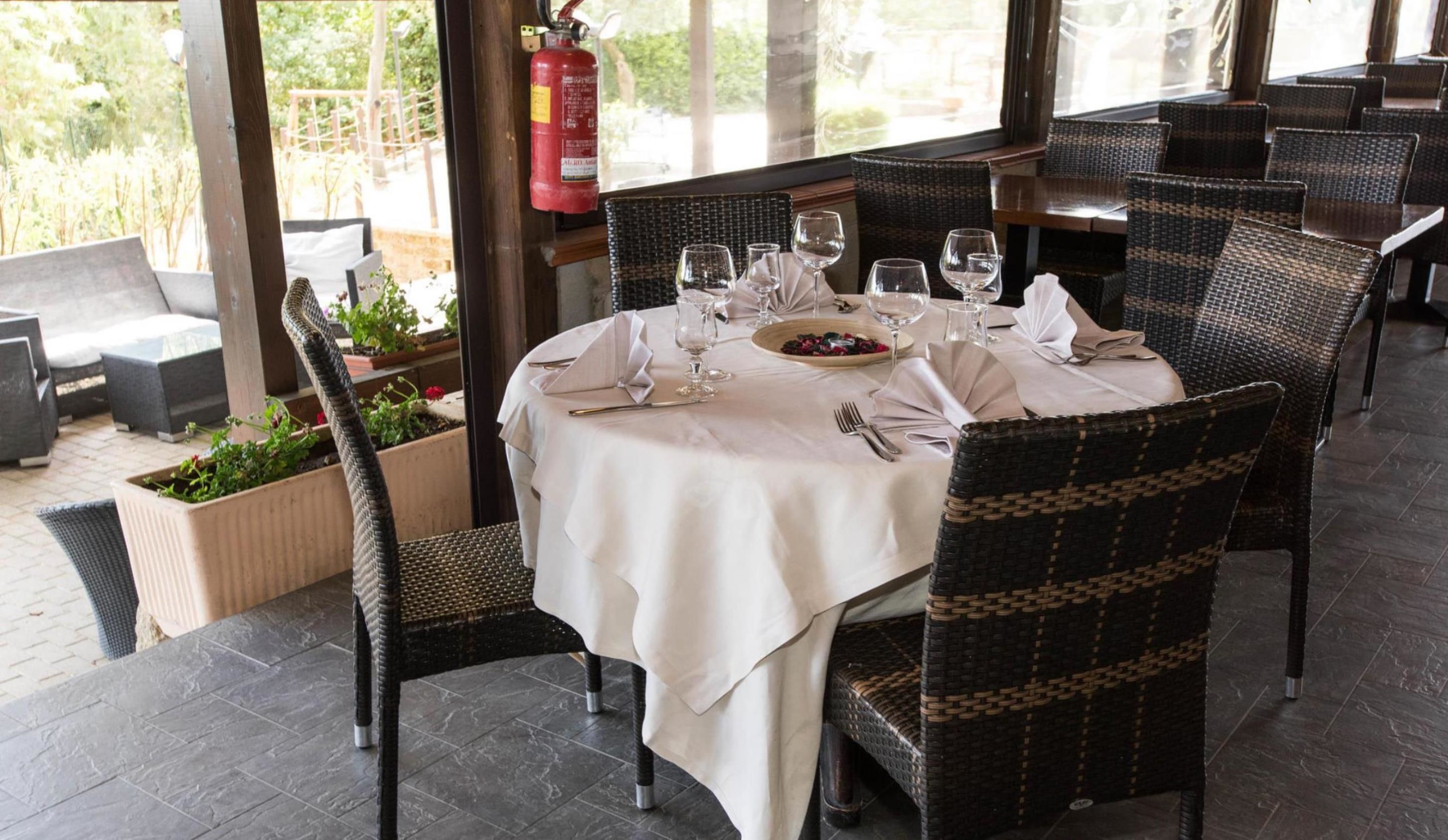 A dining area with wicker chairs and a table set for two, featuring a white tablecloth and wine glasses.