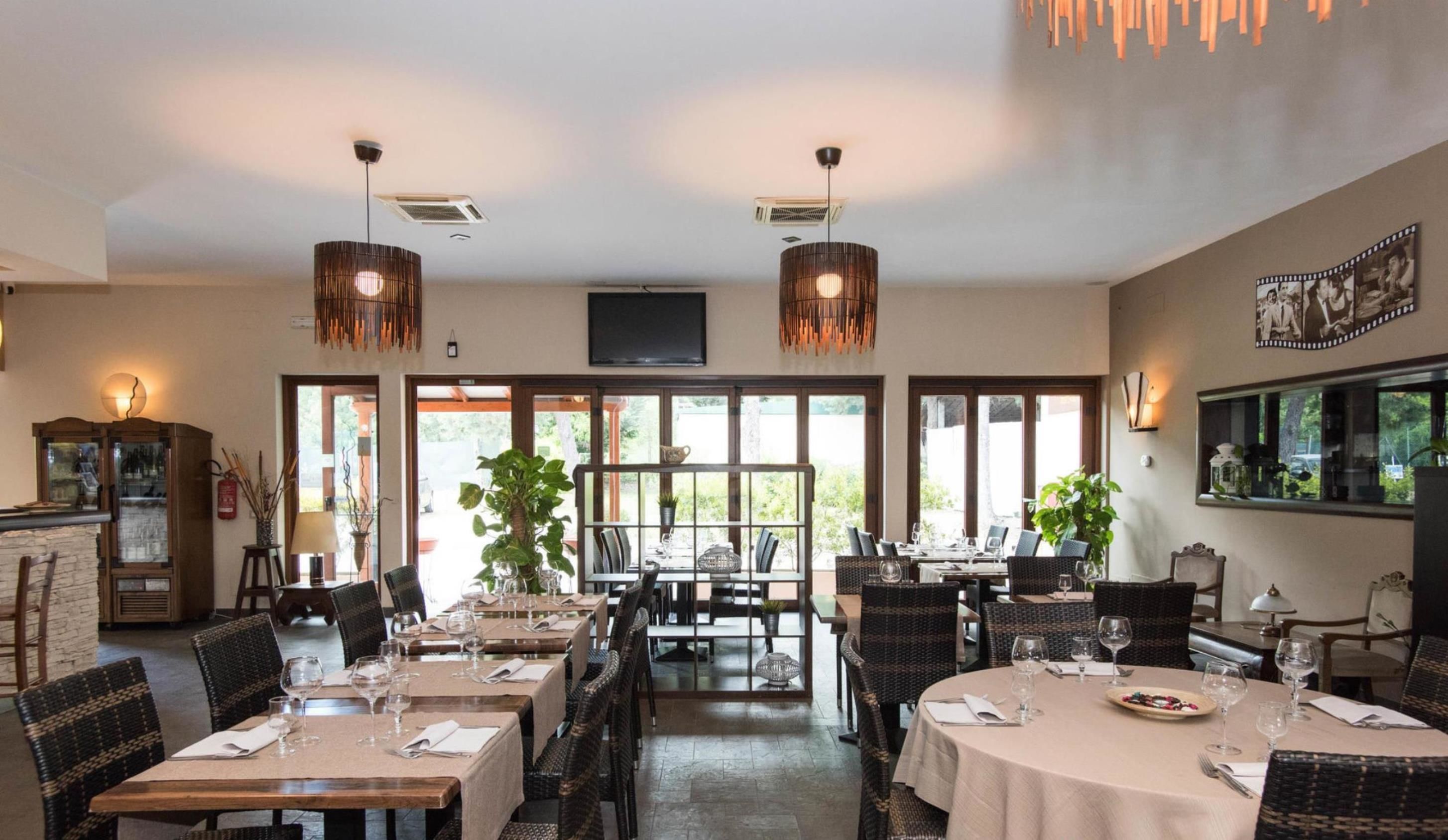 A restaurant with multiple dining tables, wicker chairs, and hanging pendant lights.