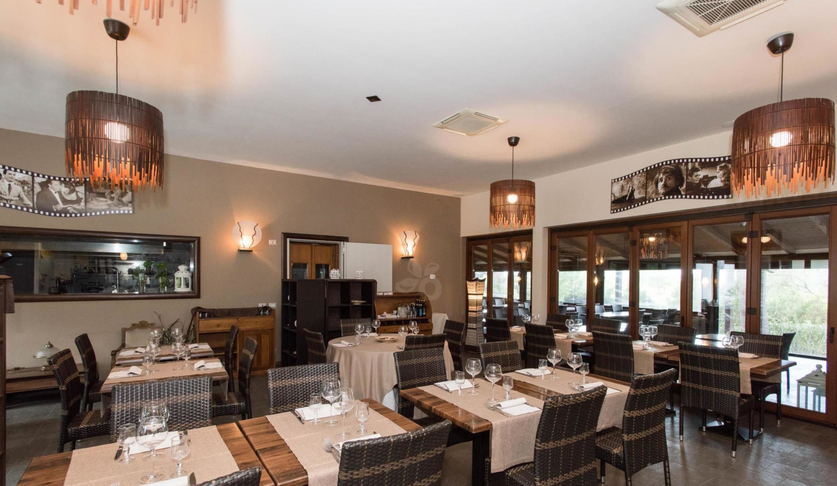 A restaurant with multiple tables and chairs, warm lighting, and large windows.