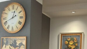 Een kamer met een groene bank, een houten klok en twee kunstwerken in lijsten.
