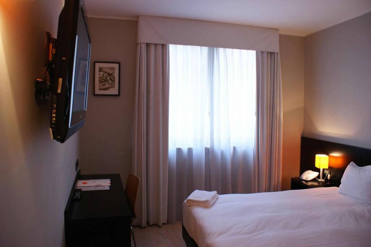 A hotel room with a bed, a desk, a television, and a window with curtains.