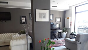 Een moderne woonkamer met een witte bank, een grijze fauteuil, een piano en een groot raam met uitzicht op de straat.