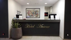 Een hotel receptie met een grote plant, een ingelijst abstract schilderij en een bordje met de tekst 'Hotel Aniene'.