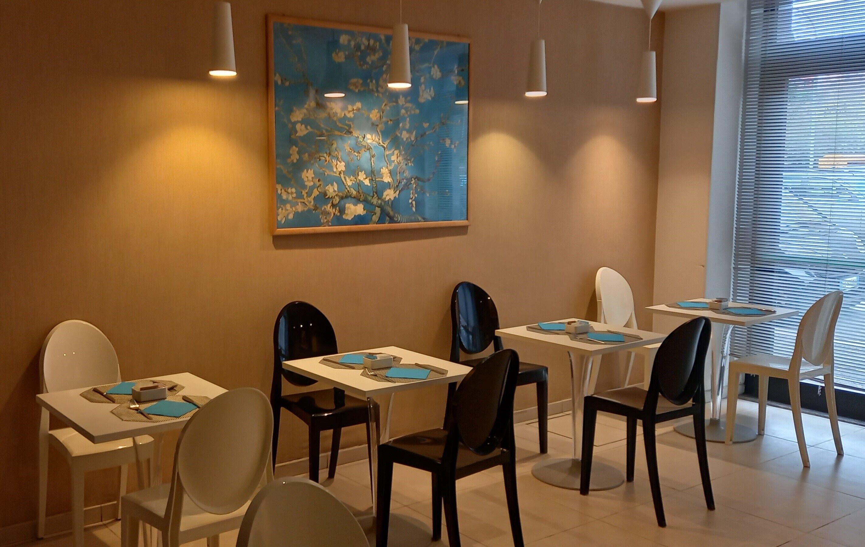 Zona pranzo con tavoli e sedie, un quadro appeso al muro e una finestra con persiane.