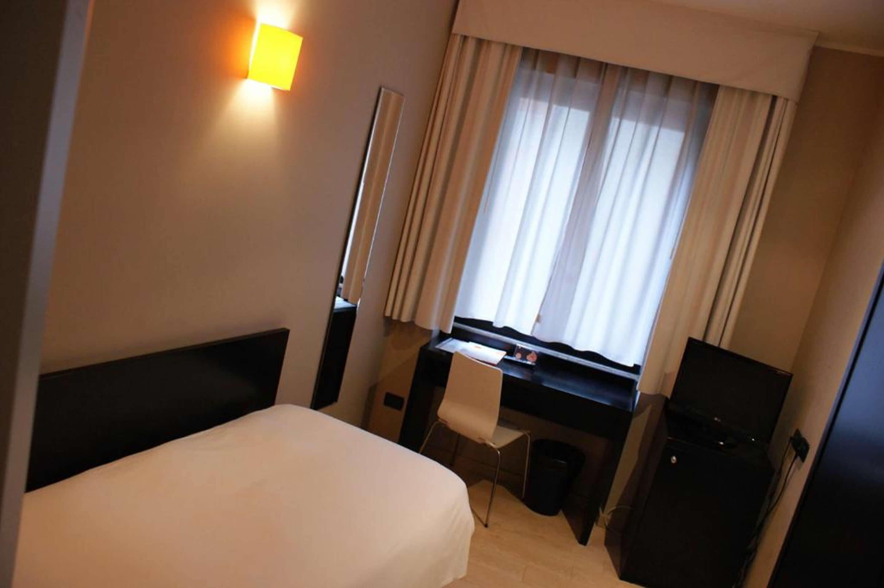 Ein Hotelzimmer mit Bett, Schreibtisch, Stuhl, Computer und Fernseher.