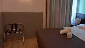 Een hotelkamer met een bed, een stoel en een nachtkastje met een lamp.