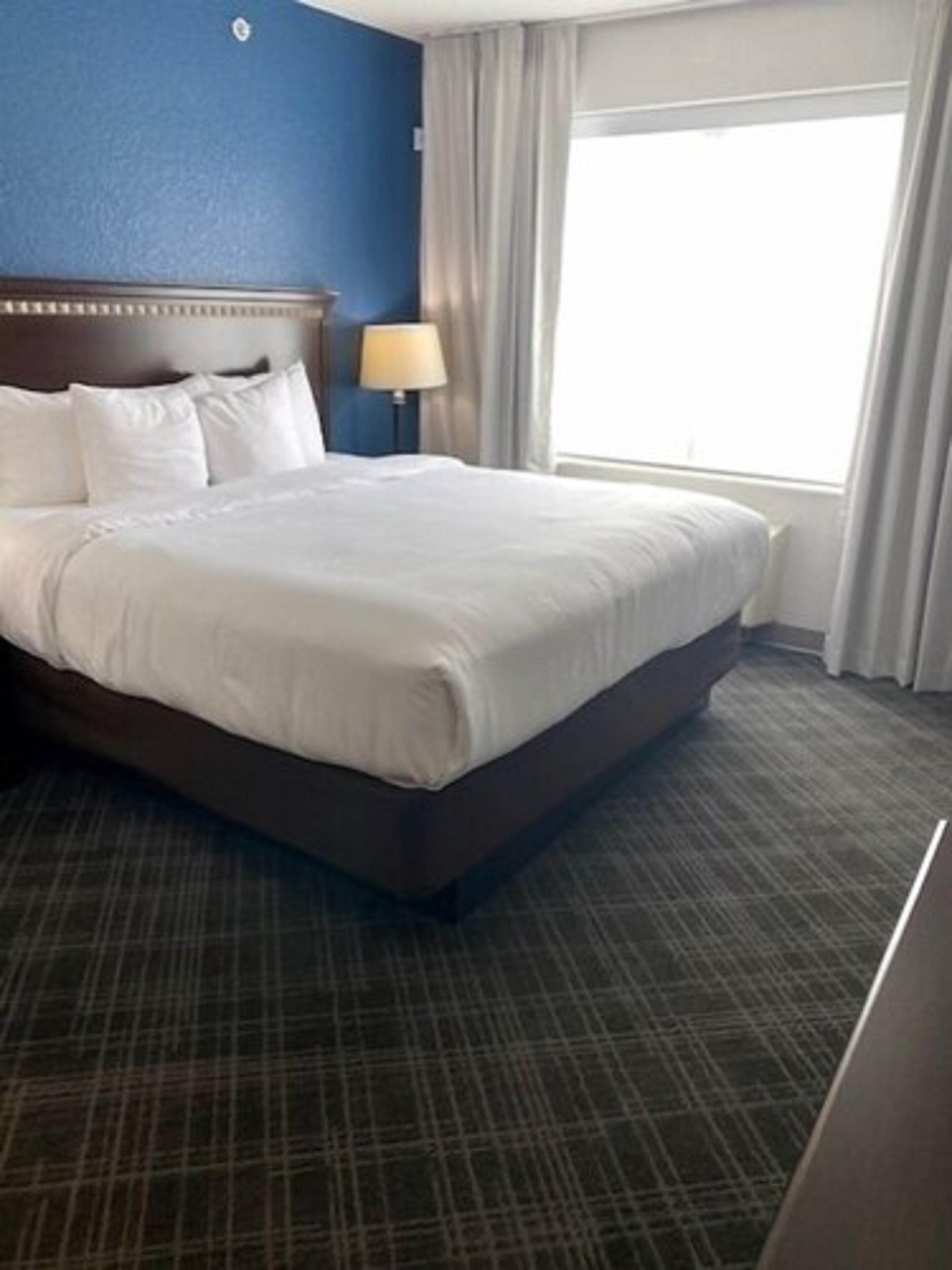 A hotel room with a large bed, a nightstand with a lamp, and a window with curtains.