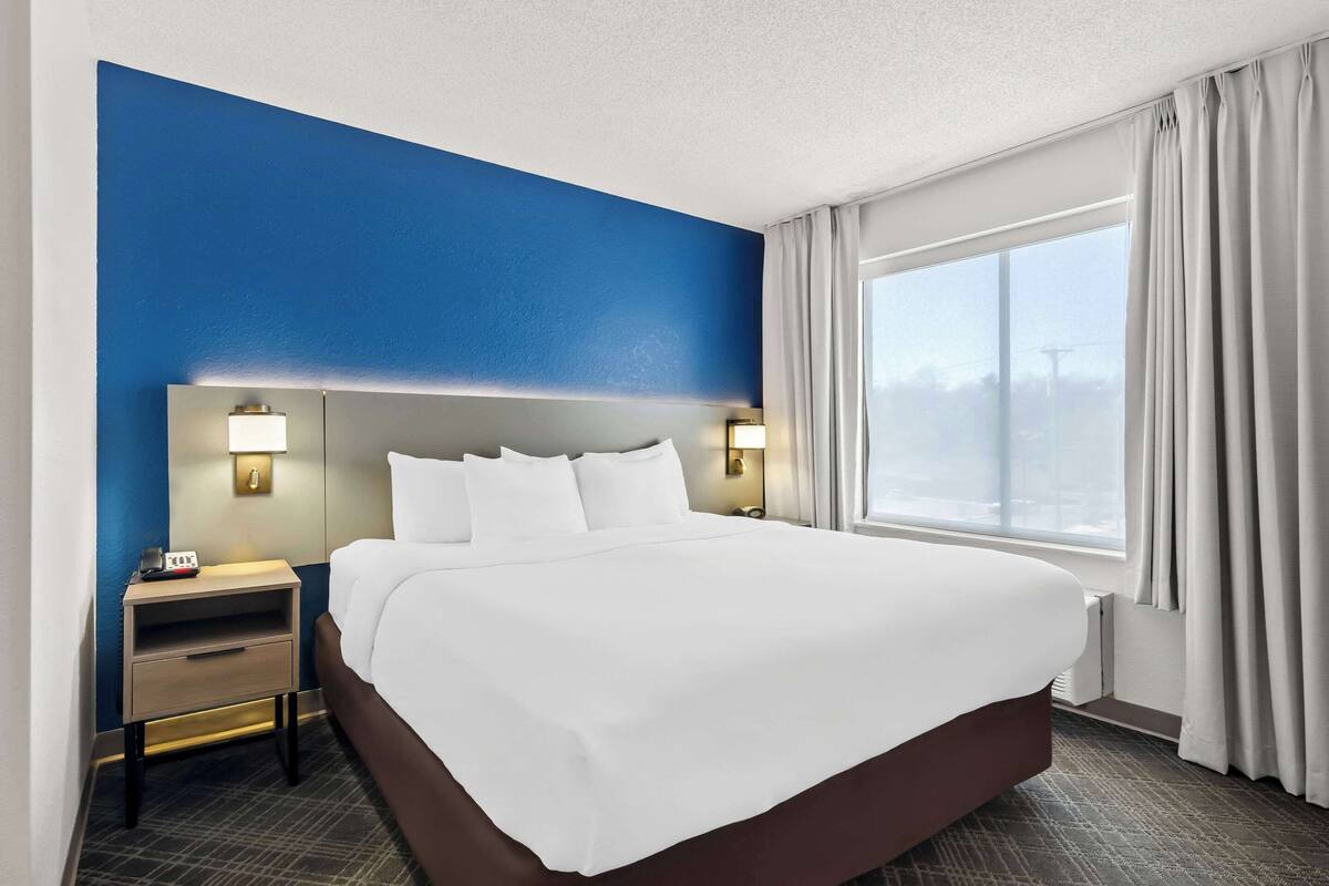 Een hotelkamer met een groot bed, twee nachtkastjes, een raam met gordijnen en uitzicht op de stad.
