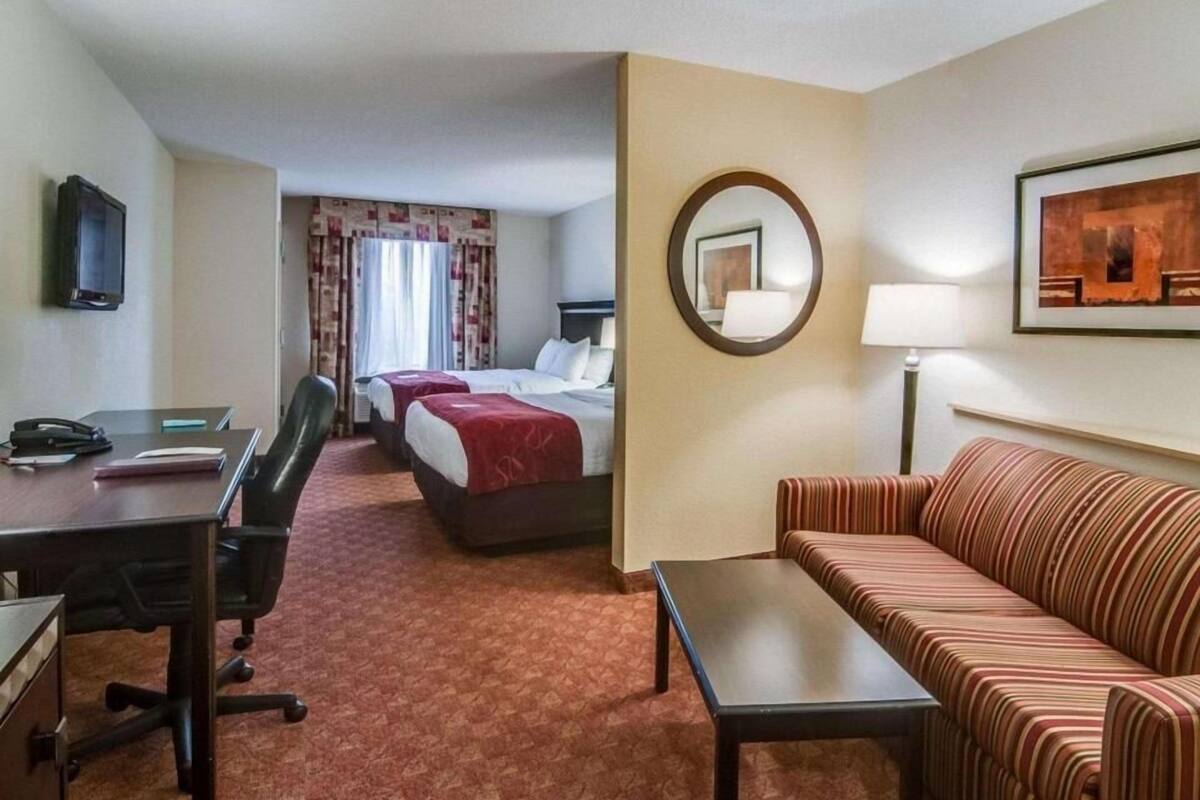 Hotelkamer met een bureau, twee bedden, een bank, een televisie, een spiegel en een lijst aan de muur.